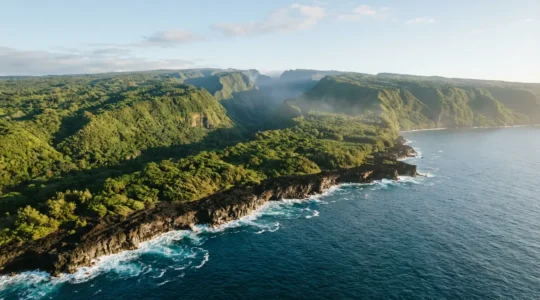 Vue aérienne spectaculaire de La Réunion montrant le littoral sauvage, les cirques verdoyants et le volcan au loin sous un ciel tropical