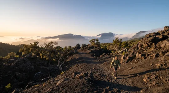 Randonneur s'entraînant sur un sentier volcanique escarpé de La Réunion avec vue sur les cirques