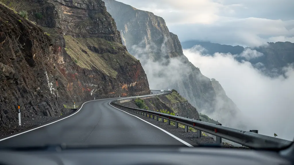 Vue grand angle depuis l'intérieur d'une voiture sur la route sinueuse de Cilaos avec focus sur le virage suivant et ravine floue en arrière-plan